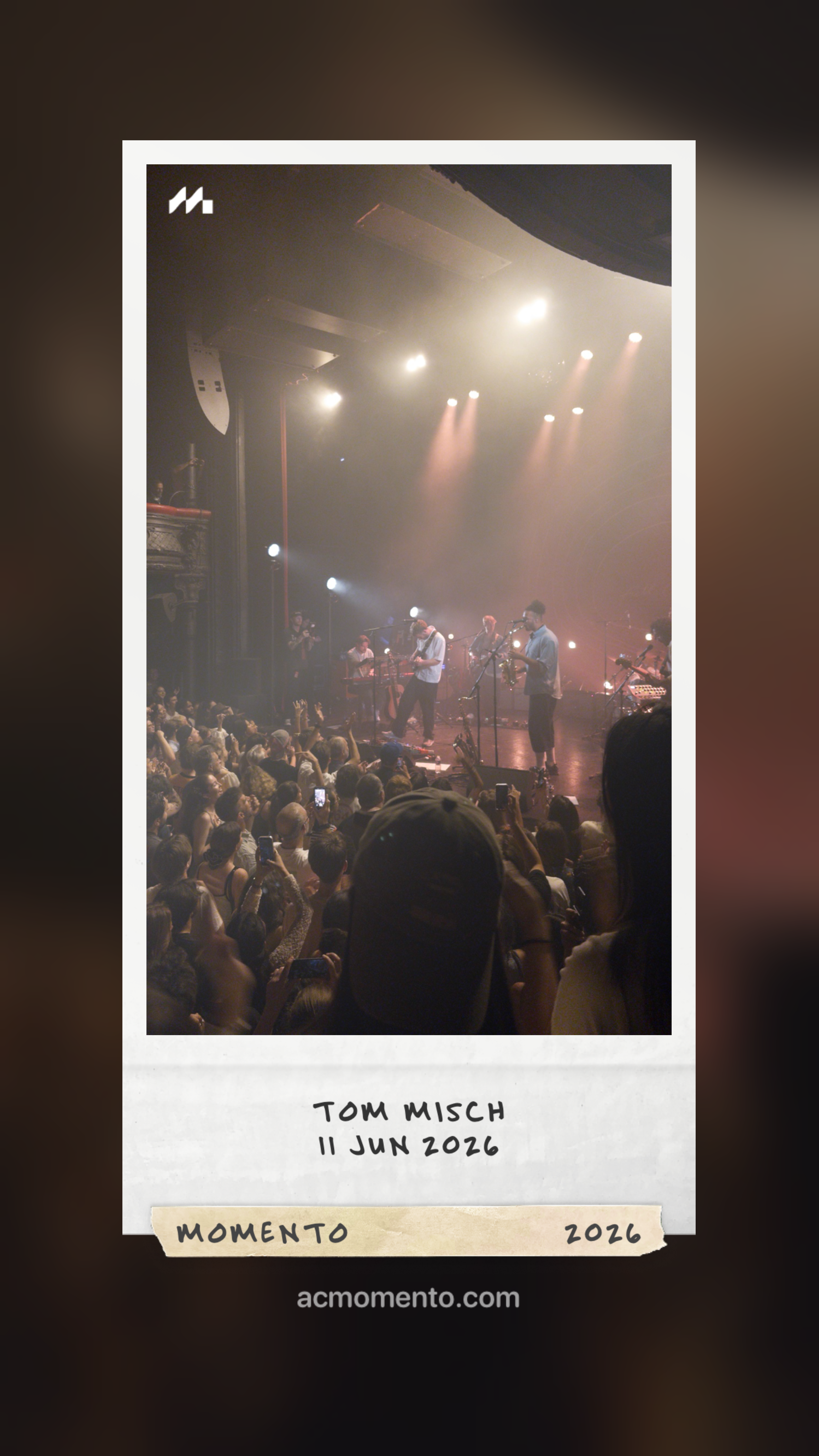 Auto-generated description: A live concert with musicians performing on stage and a crowd watching, framed as a Polaroid photo with TOM MISCH 11 JUN 2026 written at the bottom.