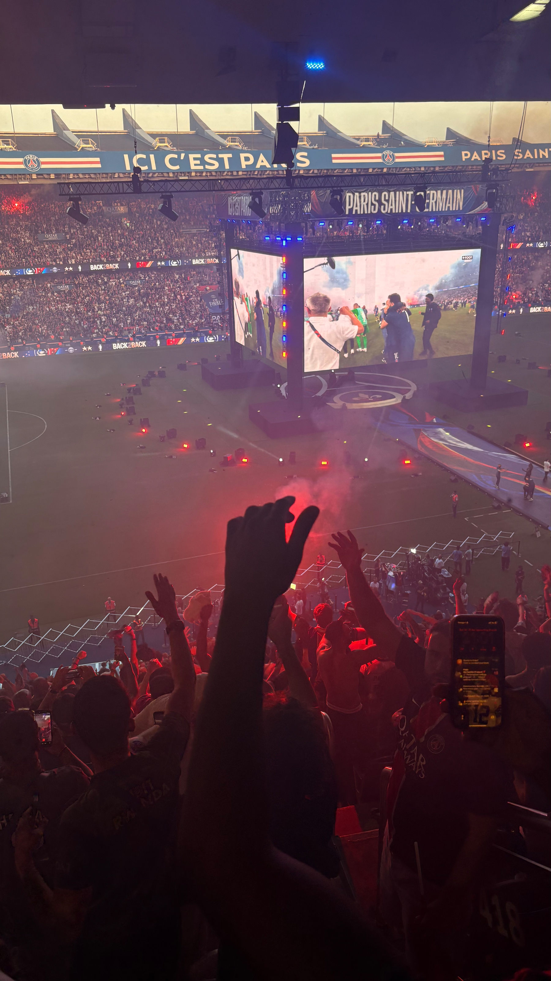 Auto-generated description: A lively football stadium scene with a cheering crowd, vibrant lights, and a large screen displaying action on the field.